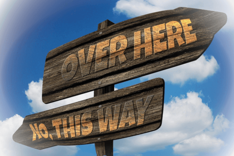 Signpost pointing in 2 different directions, one saying 'Over here', the other saying 'No, this way