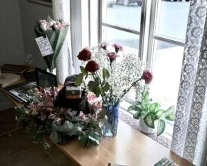 Lena's ashes on a table next to the window, but with the plastic container beautifully disguised by flowers and leaves.