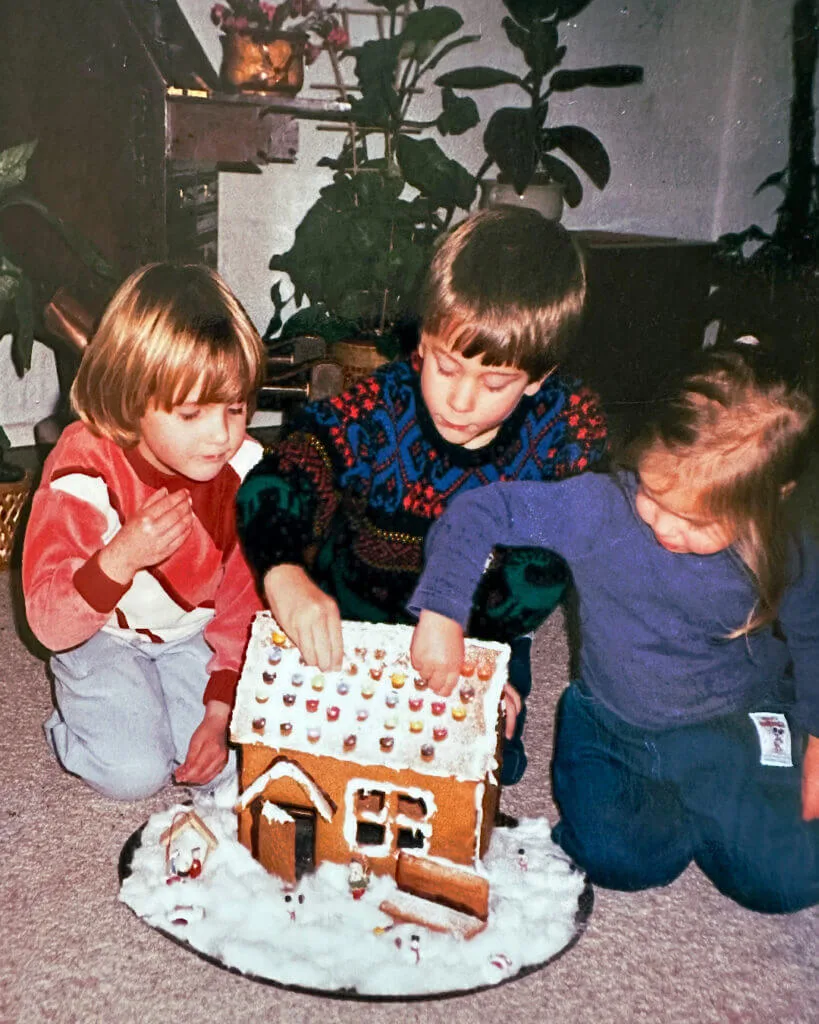 Edwin, Josie and a friend, aged around 3 and 5, kneeling on the floor, beginning to pick the Smarties off the rook off Lena's gingerbread house, now that she'd given them the go-ahead to eat it, a few days after Christmas.