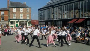 Schoolchildren country dancing in a big circle during the St George's Day celebrations outside the old Stockport Market Hall.