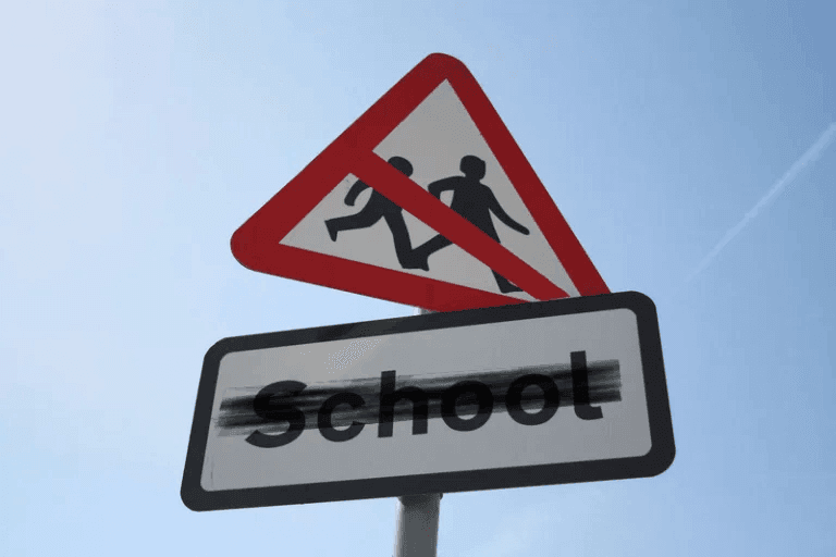 School crossing roadsigns, but with a red line cancelling the two children crossing on the sign. The word 'School' on the sign below has been mostly blacked out.