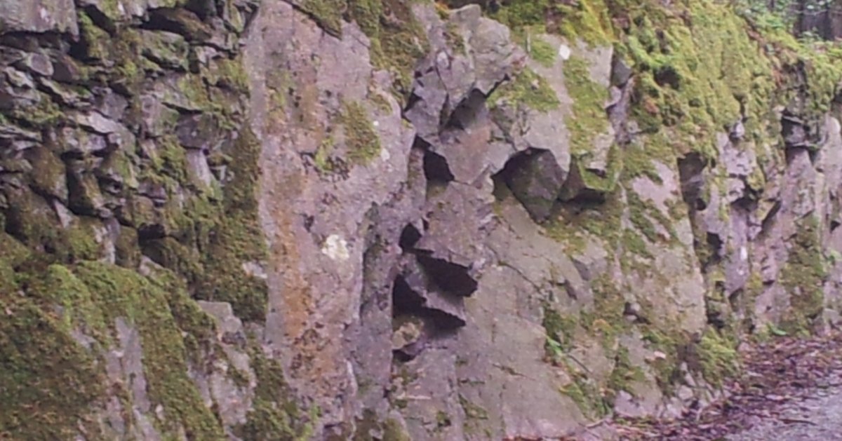At the side of the road, age has worn away the rock face. From this angle it looks like a face, with hooded eyes, a large nose and lips, peeping out from behind the wall. A goblin perhaps?