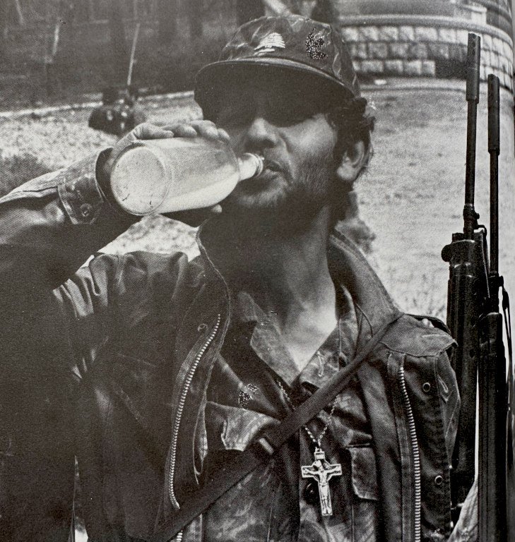 Lebanese militiaman with a large crucifix around his neck, drinking from a bottle.